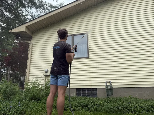 Grime Guyzz technician rinsing algae from siding on a Medina home