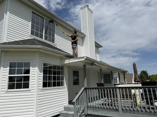 Grime Guyzz technician washing upper-story windows from a porch roof in Medina