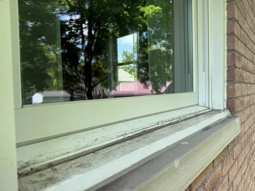 Window sill and track caked with grime before cleaning on a Medina brick home